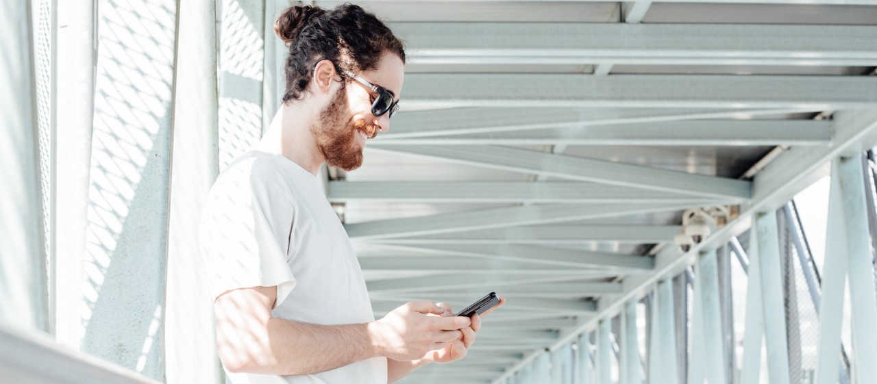 Portrait of a young man in casual clothes with a phone on the background of the modern airport terminal using smart phone. Traveler making call, messaging. Bus station. Hipster man with luggage. Copy man with luggage looking at phone on bridge 2026 09 22 17 01 14 utc cr